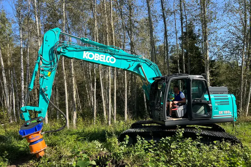 Excavator clearing undergrowth at the edge of pine woods