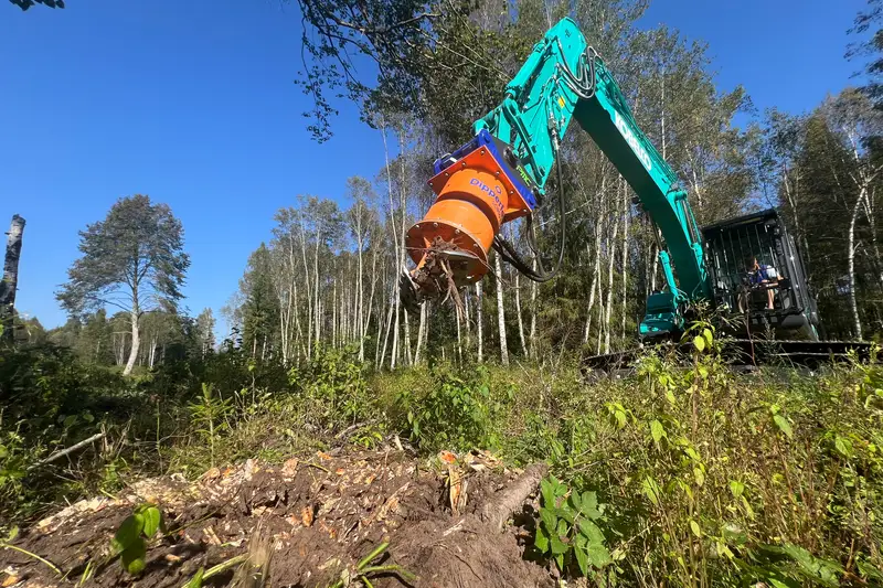 Excavator with a grinding head clearing brush and stumps from a wooded lot